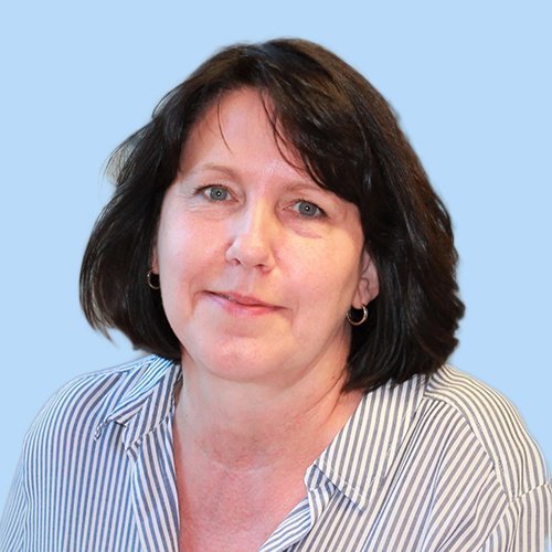 Eine Frau mit dunklen, schulterlangen Haaren lächelt freundlich vor einem hellblauen Hintergrund.